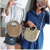 A woman holds a handwoven straw moon bag with a top handle against a blue shirt.