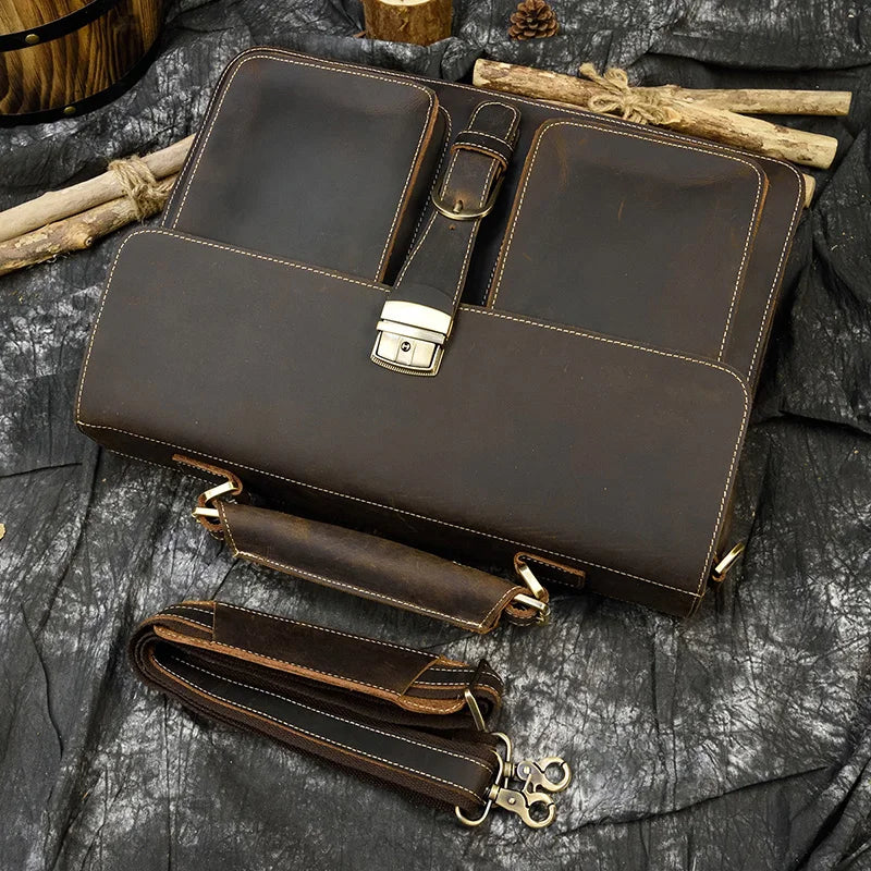 A dark brown vintage Crazy Horse leather briefcase with a laptop compartment and leather strap lying on a dark fabric.