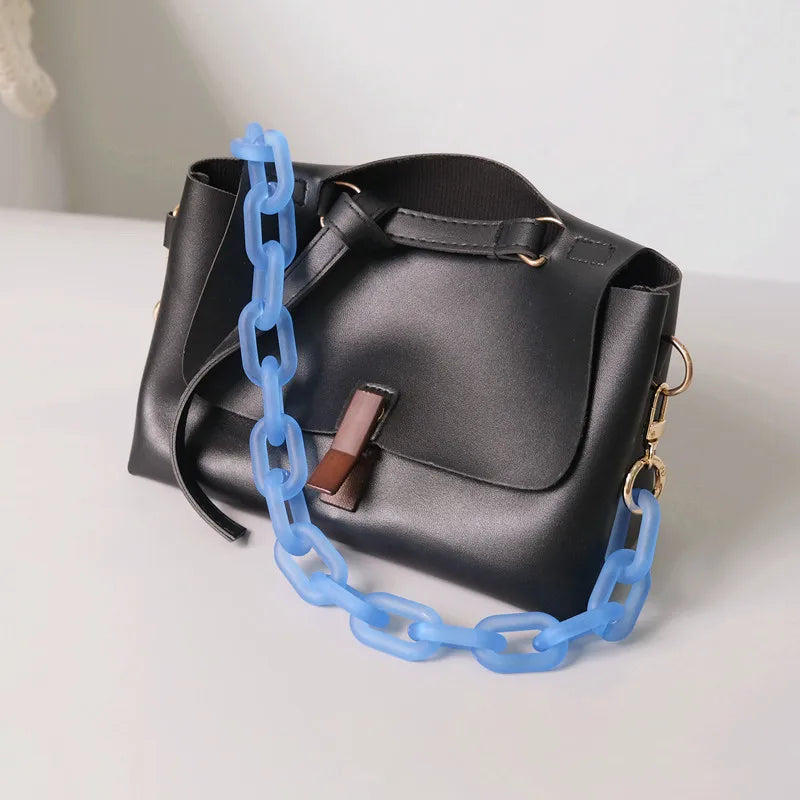 A black shoulder bag with a flap and gold hardware is shown with a bright blue chain strap.