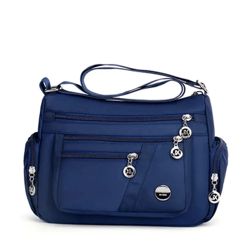 A navy blue waterproof nylon crossbody tote bag with silver hardware.
