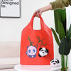 Un sac de shopping rouge vif avec des illustrations de pandas, tenu par une main à côté d'une grande plante verte.
