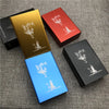 Three custom engraved cigarette cases in gold, red, and blue are displayed on a gray fabric surface.