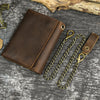 A brown genuine leather trifold wallet with a detachable gold-toned chain lying on a gray textured surface.