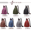 A variety of colored canvas backpacks including purple, green, black, brown, dark blue, gray, and red.