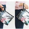 Una persona sostiene una bolsa de cosméticos transparente con estampado de hoja tropical.
