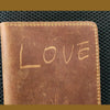 A brown leather passport wallet with the word LOVE embossed on the cover, set against a dark textured background.