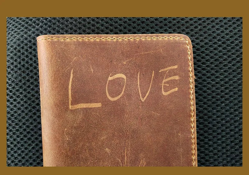 A brown leather passport wallet with the word LOVE embossed on the cover, set against a dark textured background.