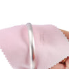 A close-up of a pink polishing cloth being used to clean silver and gold jewelry.