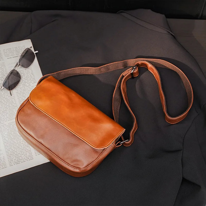 A brown retro PU leather crossbody shoulder bag resting on a dark fabric next to sunglasses and a piece of paper.