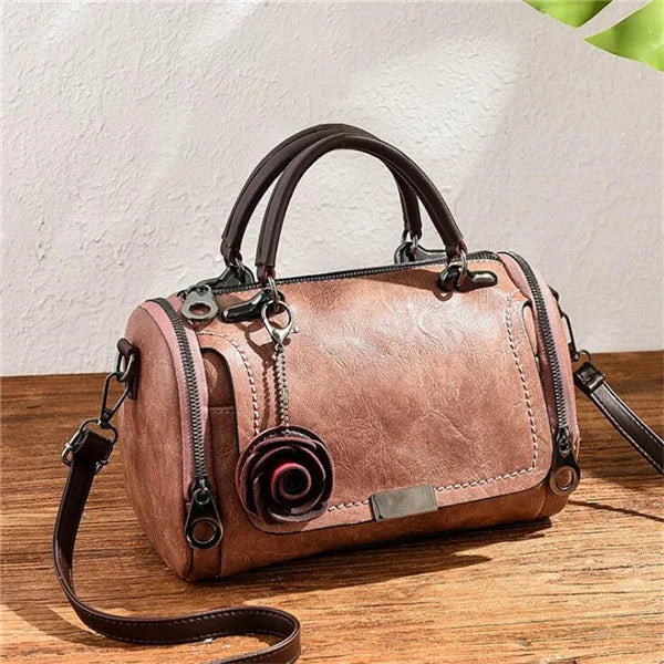 Braune Leder-Blumen-Anhänger-Schultertasche mit dunklem Riemen auf Holzoberfläche.