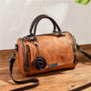 Braunes Leder-Blumen-Anhänger-Schultertasche mit dunkelbranem Riemen auf Holzoberfläche.
