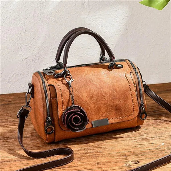 Braunes Leder-Blumen-Anhänger-Schultertasche mit dunkelbranem Riemen auf Holzoberfläche.