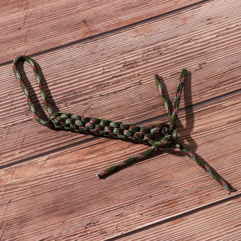 A green and pink 7-strand paracord rope tied into a knot, lying on a wooden surface.