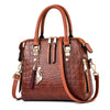 A brown crocodile-embossed leather tassel shoulder bag with gold hardware and a leather strap.