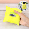 Une main tient un sac de shopping jaune vif et pliable écologique avec une étiquette noire sur une surface en bois clair.