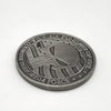 A round, dark silver commemorative coin featuring a stylized skull and crossbones design surrounded by text.