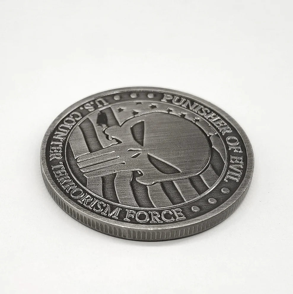 A round, dark silver commemorative coin featuring a stylized skull and crossbones design surrounded by text.