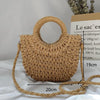 A handwoven straw moon bag with a top handle and strap is displayed on a white surface.