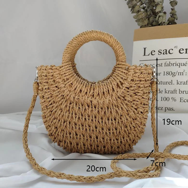 A handwoven straw moon bag with a top handle and strap is displayed on a white surface.