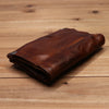 Dunkelbraunes Vintage-Leder-Bifold-Wallet auf einer hellen Holzoberfläche.