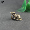 A vintage brass figurine of a rat is placed on a dark surface next to green leaves.