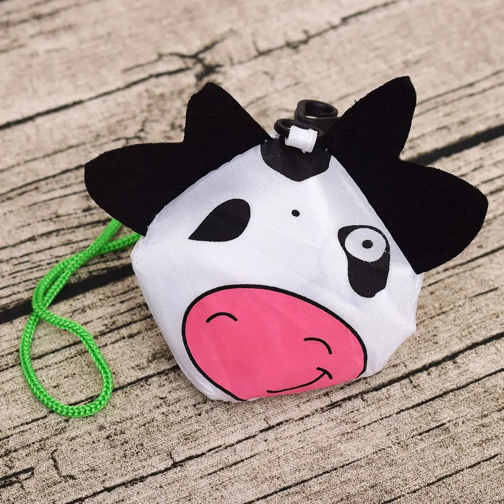 Visage de vache en dessin noir et blanc, fait de tissu blanc avec des accents roses, attaché à un cordon vert.