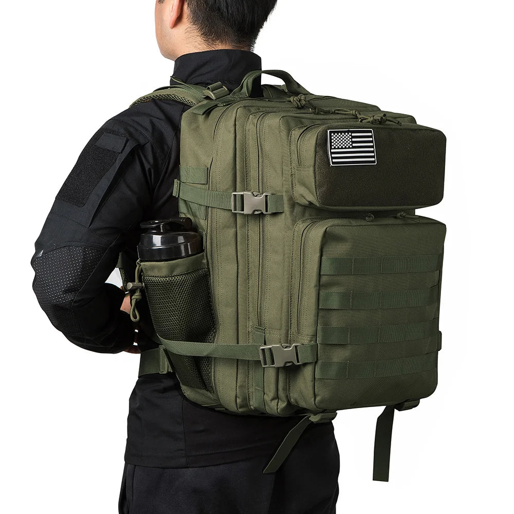 A person is wearing a olive green tactical backpack with a MOLLE system and a flag patch on the front.