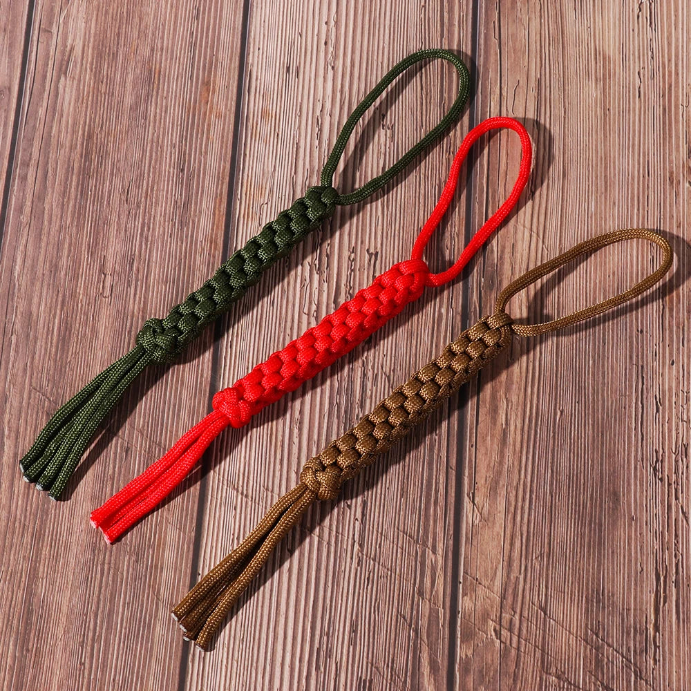 Three paracord keychains in green, red, and brown are displayed on a wooden surface.
