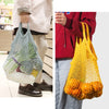 A bright yellow mesh grocery tote bag filled with oranges, held by a person.