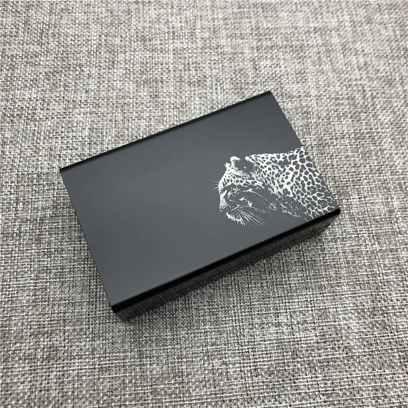 A black custom engraved cigarette case featuring a silver leopard print design on a textured gray fabric.