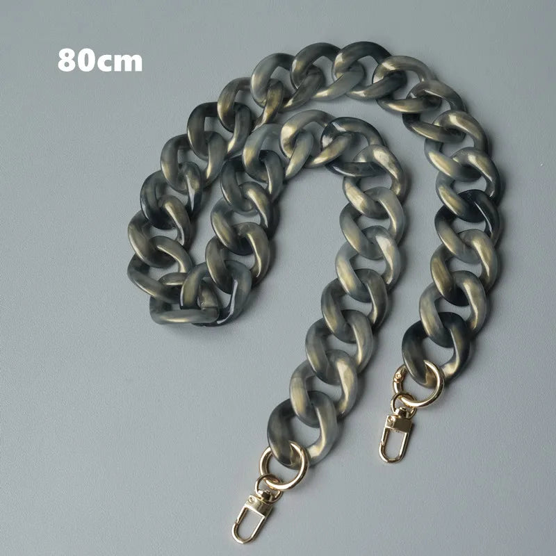 Bolso de cadena de hombro de resina plateada con diseño de eslabones, mostrado contra un fondo gris.