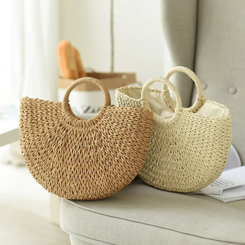 Two natural straw moon bags with top handles resting on a light-colored sofa.