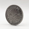 A round, dark silver commemorative coin featuring a stylized skull and crossbones design.