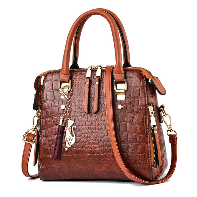 A brown crocodile-embossed leather tassel shoulder bag with gold hardware and a brown strap.