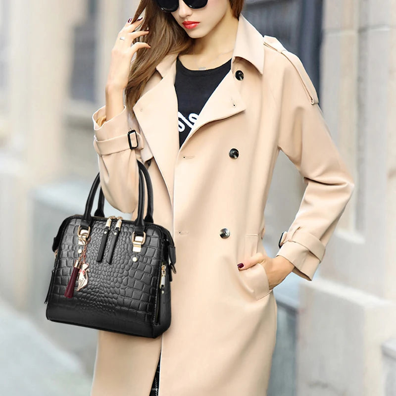 A woman wearing a beige trench coat holds a black crocodile-embossed leather tassel shoulder bag.
