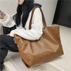A woman holds an oversized brown PU leather tote bag with a zipper closure.