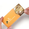 A hand holds an orange RFID blocking card sleeve, which is placed over a gold credit card.