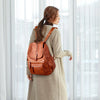 A woman wearing a beige coat carries a brown vintage soft leather backpack.