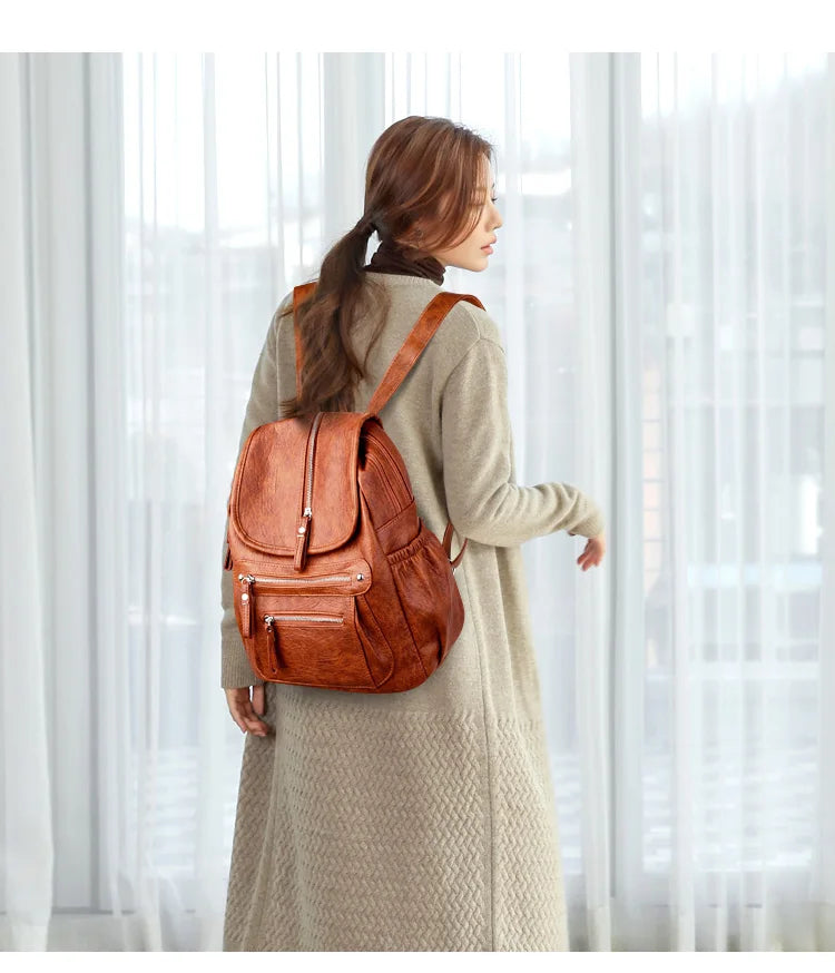 A woman wearing a beige coat carries a brown vintage soft leather backpack.
