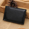 A black men's leather money clip wallet resting on a wooden surface next to a pinecone.