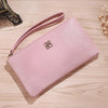 Cartera de cuero sintético rosa claro con cremallera y correa, tumbada sobre una superficie de madera.