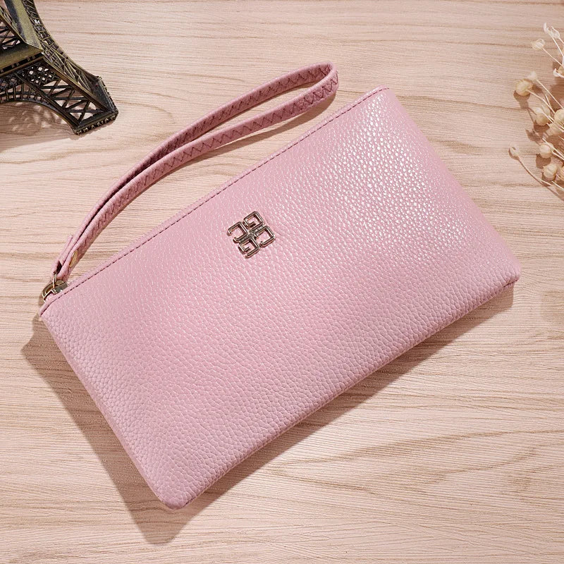 Cartera de cuero sintético rosa claro con cremallera y correa, tumbada sobre una superficie de madera.