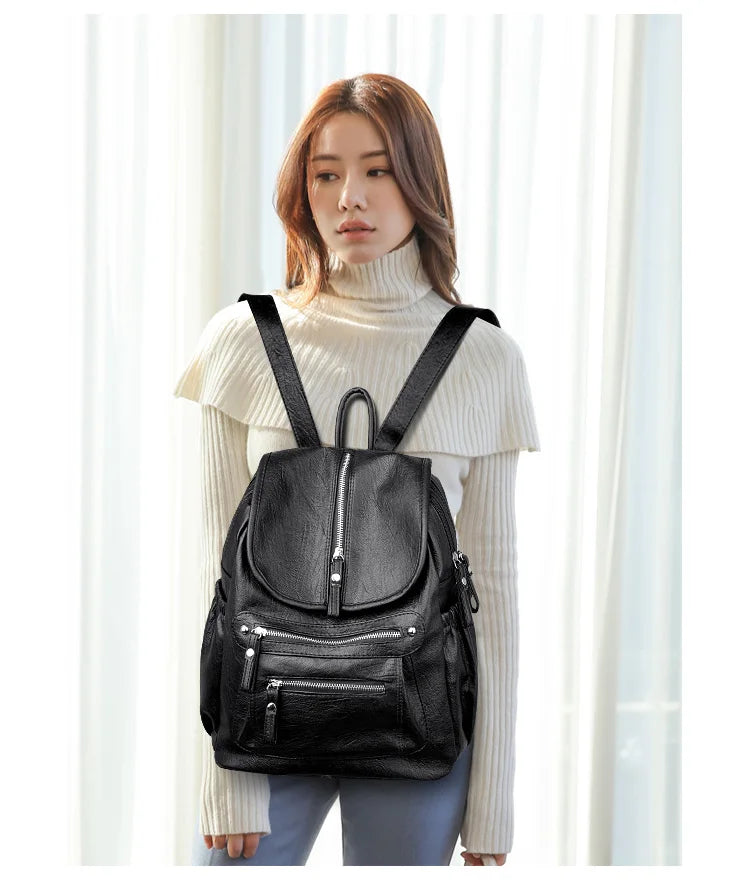 A woman wearing a black vintage soft leather backpack and a cream turtleneck sweater.