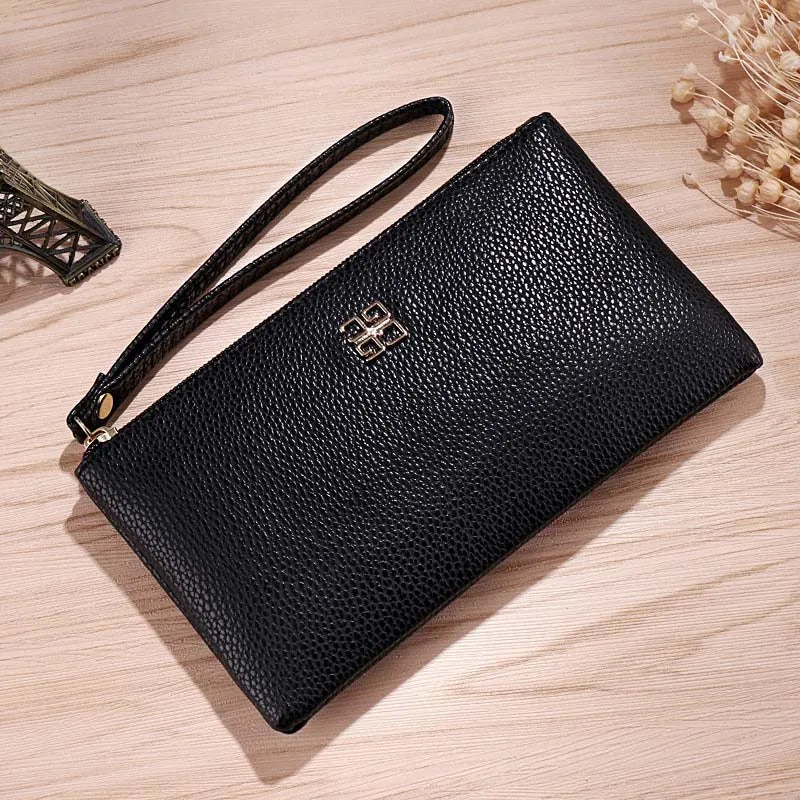Cartera con cremallera de cuero sintético negro y correa de cuero, tumbada sobre una superficie de madera clara.