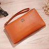 Cartera con cremallera de cuero PU marrón y correa de cuero sobre una superficie de madera clara.