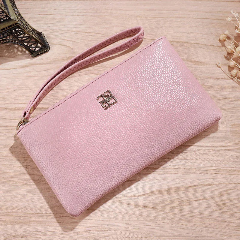 Cartera de cuero sintético rosa claro con cremallera, sobre una superficie de madera con un accesorio metálico decorativo cer