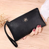 Cartera con cremallera de cuero sintético negro apoyada sobre una superficie de madera, sostenida por una mano.