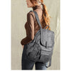 A woman wearing a brown turtleneck and dark jeans is shown carrying a gray vintage soft leather backpack.