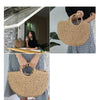 A woman holds a large, handwoven straw moon bag with a top handle against a light background.