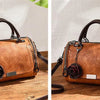 Braunes Leder-Blumen-Anhänger-Schultertasche mit dunklem Riemen auf Holzoberfläche.